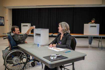A un bureau de vote, une personne handicapée remet son bulletin de vote dans une urne.
