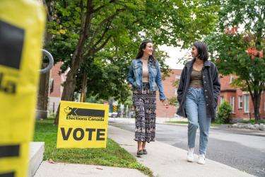 Des électrices qui se dirigent vers un lieu de scrutin en suivant les affiches Vote d’Élections Canada qui indiquent l’endroit du bureau de scrutin.