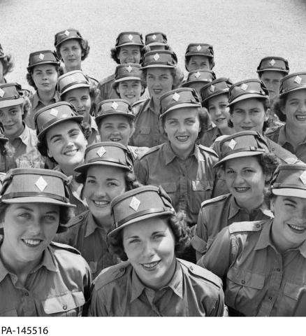Photographie en noir et blanc d’un grand groupe de femmes en uniforme militaire souriant à la caméra.