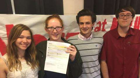 Photographie de quatre adolescents souriants tenant un morceau de papier.