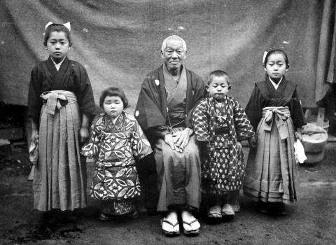 CE33-Japanese-alt 1 Photographie en noir et blanc de cinq membres d’une famille japonaise en tenue traditionnelle. Un homme plus âgé est assis au milieu, entouré de deux enfants.
