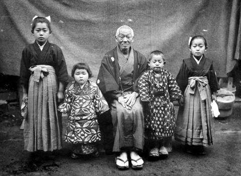 Photographie en noir et blanc de cinq membres d’une famille japonaise en tenue traditionnelle. Un homme plus âgé est assis au milieu, entouré de deux enfants.