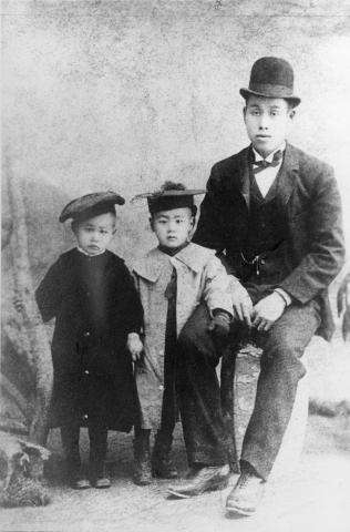 Photographie en noir et blanc d’un homme japonais assis à côté de ses deux jeunes enfants.