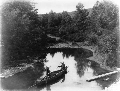 Image en noir et blanc de deux hommes autochtones dans un canot d’écorce à Restigouche, au Québec.
