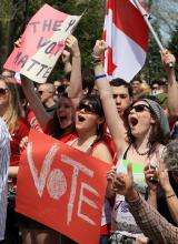 00-Context-card-Youth_FR Photographie d’un groupe de jeunes manifestants brandissant des drapeaux canadiens et des pancartes indiquant en anglais « Vote » La traduction : « Votez »
