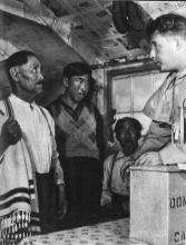VRTT_Inuit_1953_FR Photographie en noir et blanc prise au Labrador (Nunatsiavut) lors d'une élection. Joe Millik prête serment comme fonctionnaire électoral devant le directeur du scrutin Harry Nosworthy.