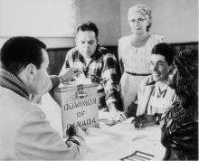 VRTT_FNP_1962_FR Photographie en noir et blanc du conseil de Hiawatha à l’occasion d’une élection partielle fédérale. Les premiers votes exprimés après que le droit de vote ait été octroyé à tous les Indiens inscrits ont été ceux de la bande de Rice Lake, près de Peterborough, en Ontario. De droite à gauche : Lawrence Salleby; chef Ralph Loucks, scrutateur; Lucy Muskrat, greffière du scrutin; Eldon Muskrat, travailleur électoral.